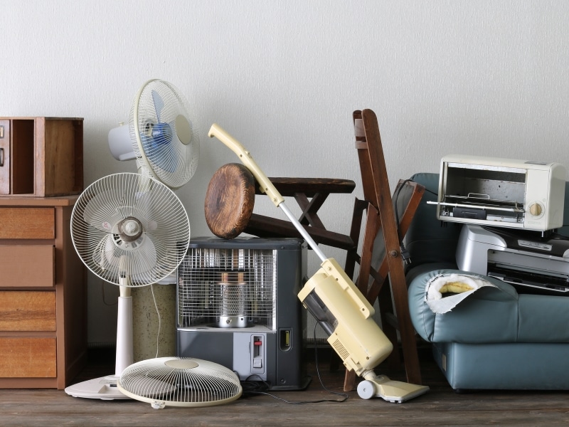 A cluttered room shows items being gathered while clearing out a deceased estate. There are fans, furniture, and appliances.